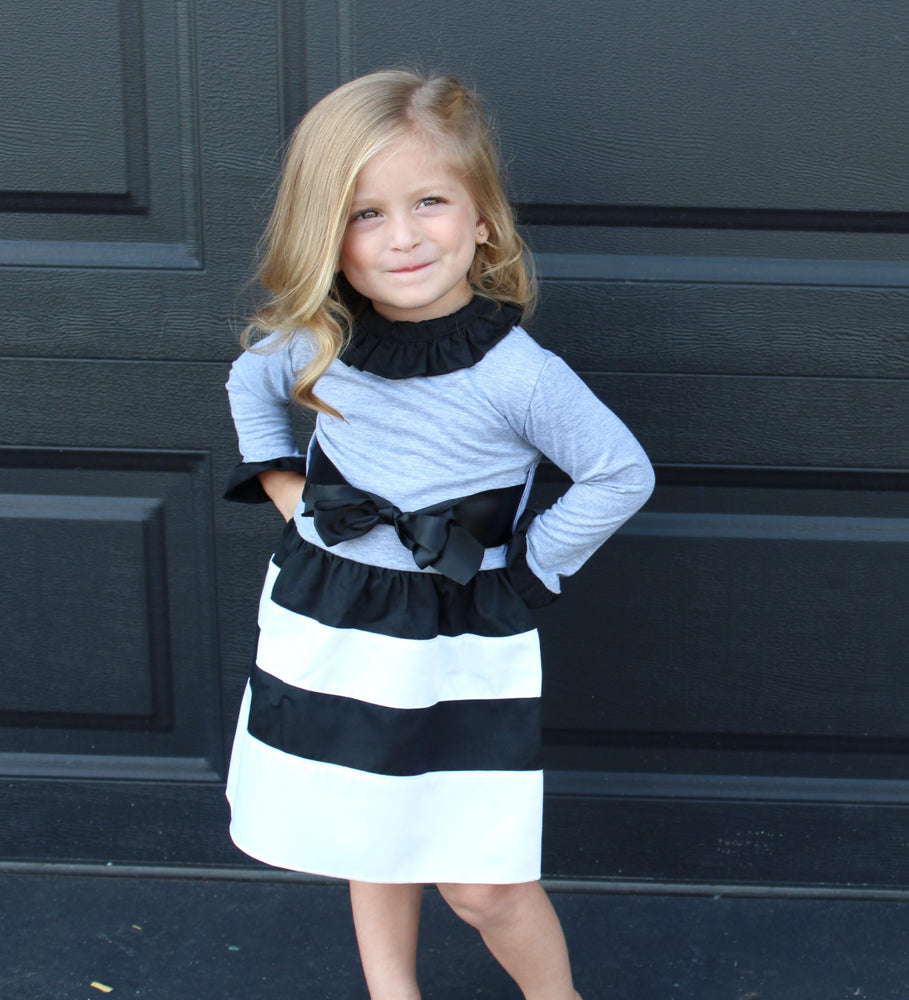 Black, grey and white long sleeved dress with ruffle sleeaves and collar. A thick ribbon slides around the waist and ties in a big bow. 